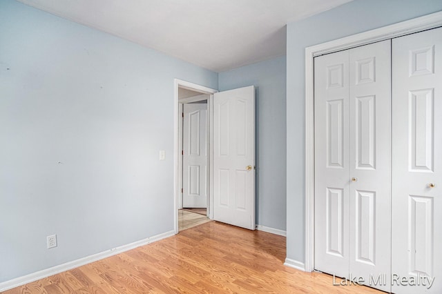 unfurnished bedroom with light wood-type flooring, a closet, and baseboards