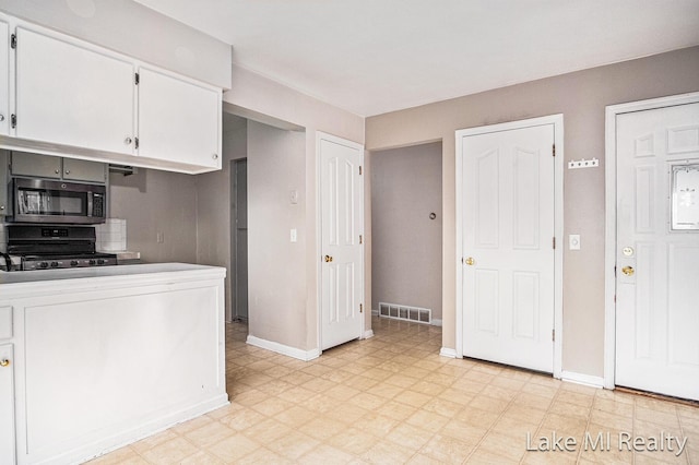 kitchen featuring stainless steel microwave, black range, light flooring, white cabinets, and baseboards