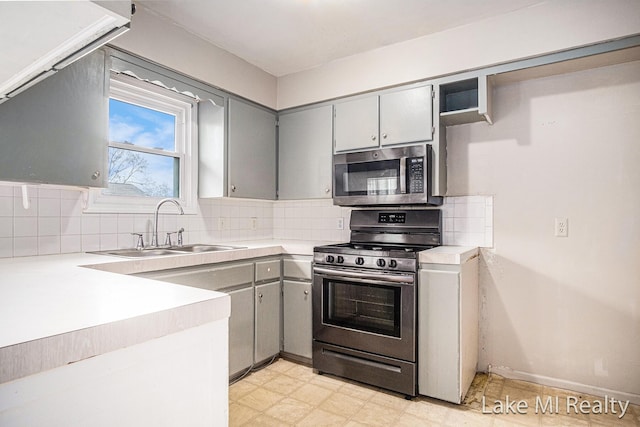 kitchen with appliances with stainless steel finishes, gray cabinets, a sink, tasteful backsplash, and light floors