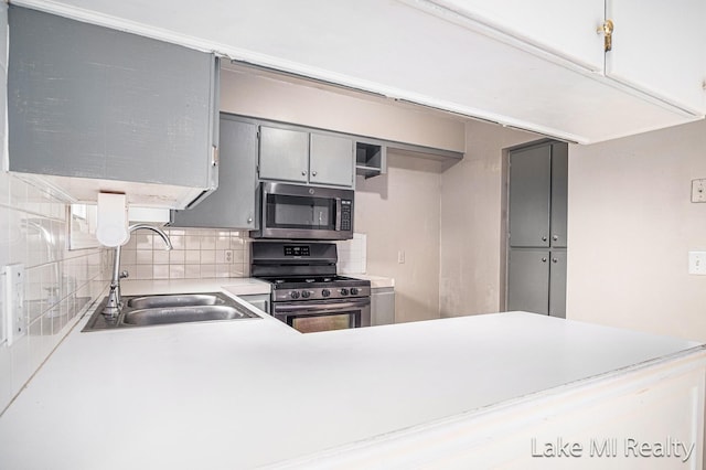 kitchen featuring stainless steel appliances, a sink, gray cabinets, tasteful backsplash, and light countertops