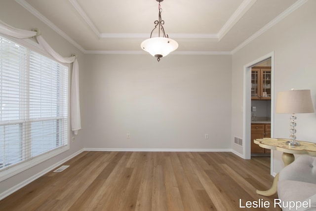 unfurnished dining area with healthy amount of natural light, light wood-style flooring, a tray ceiling, baseboards, and crown molding