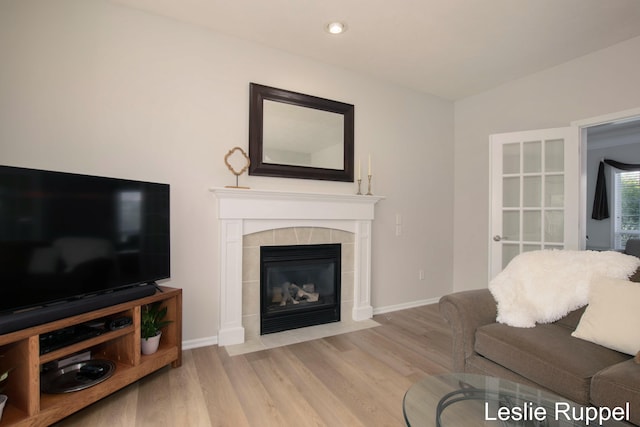 living area with wood finished floors, a tile fireplace, and baseboards