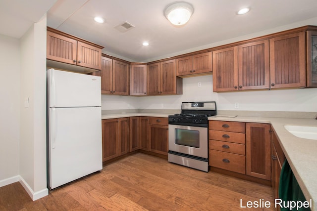 kitchen with freestanding refrigerator, stainless steel range with gas stovetop, light wood-style flooring, light countertops, and recessed lighting