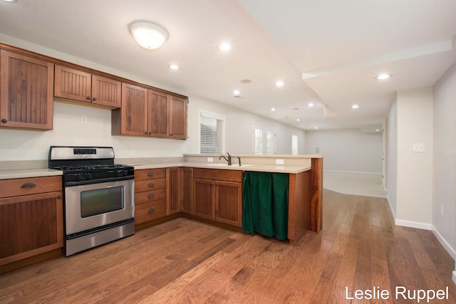 kitchen with gas stove, a peninsula, wood finished floors, light countertops, and baseboards