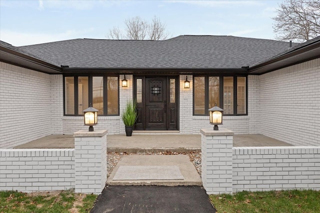 property entrance with covered porch, brick siding, and a shingled roof