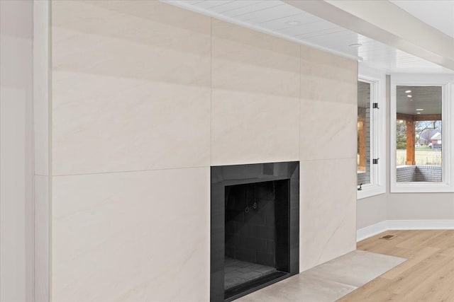 detailed view of a tiled fireplace, wood finished floors, and baseboards