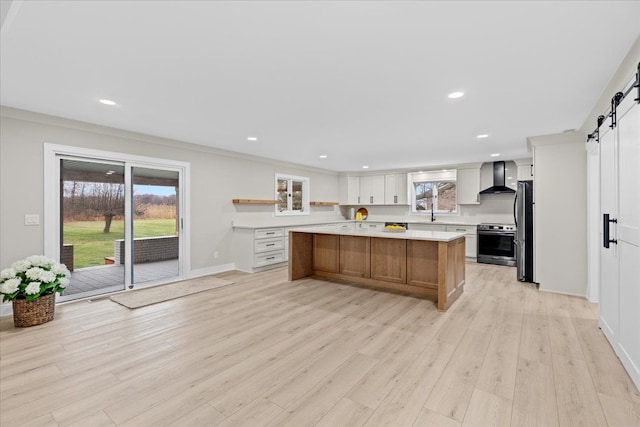 kitchen featuring wall chimney range hood, a barn door, stainless steel appliances, light countertops, and light wood finished floors