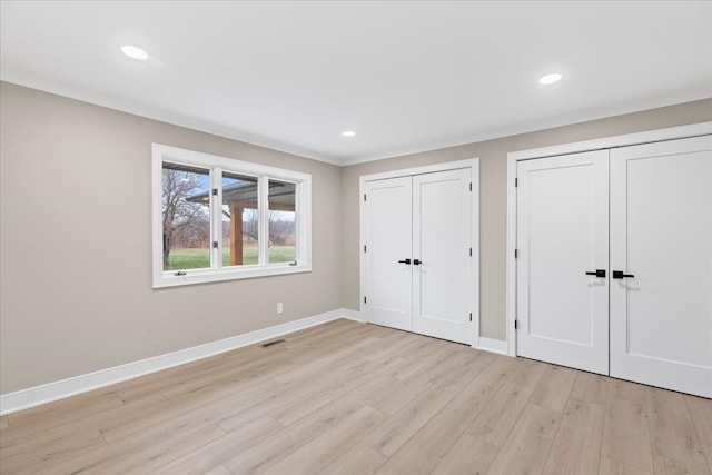 unfurnished bedroom featuring two closets, light wood-style floors, baseboards, and recessed lighting