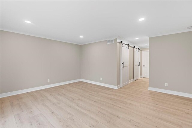 spare room featuring a barn door, light wood finished floors, ornamental molding, baseboards, and recessed lighting