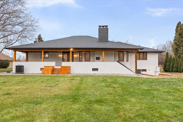back of house with a chimney, a lawn, brick siding, and central AC unit
