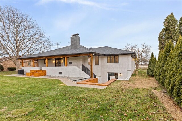 rear view of property featuring a chimney, central AC, a yard, brick siding, and a patio