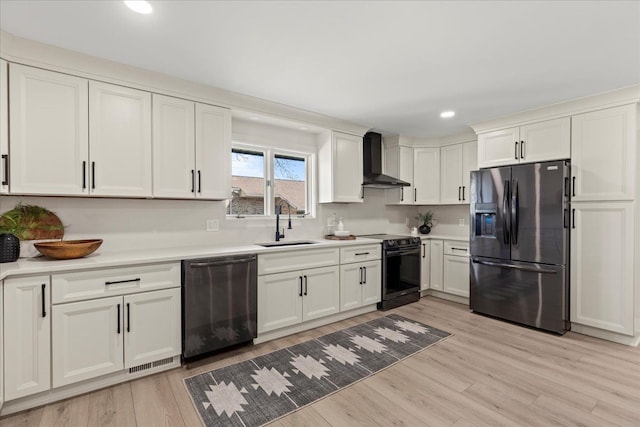 kitchen featuring black appliances, wall chimney exhaust hood, a sink, light wood finished floors, and light countertops