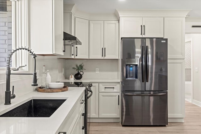 kitchen featuring stainless steel fridge, extractor fan, light countertops, light wood-style floors, and white cabinetry