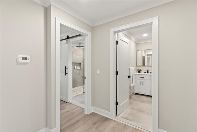 corridor featuring a barn door, light wood-style floors, baseboards, and ornamental molding