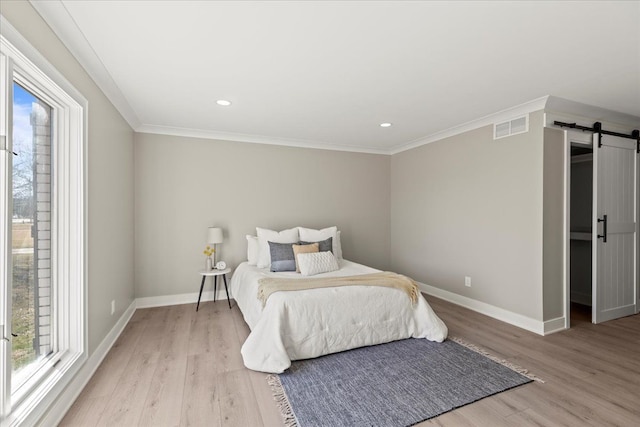 bedroom featuring a barn door, light wood-style flooring, baseboards, crown molding, and recessed lighting
