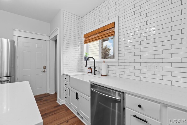 kitchen with appliances with stainless steel finishes, a sink, light countertops, tasteful backsplash, and white cabinets