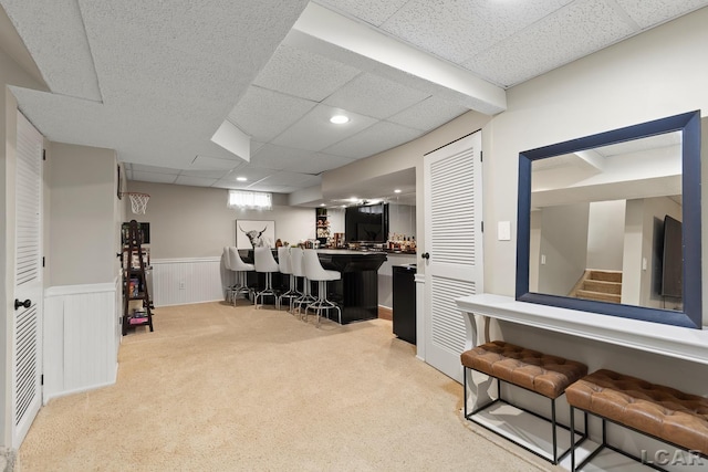 office area featuring wet bar, a drop ceiling, light colored carpet, recessed lighting, and a wainscoted wall