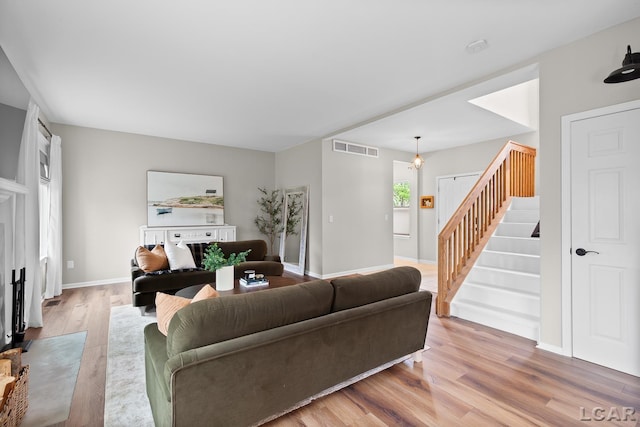 living room with stairs, light wood-style flooring, and baseboards