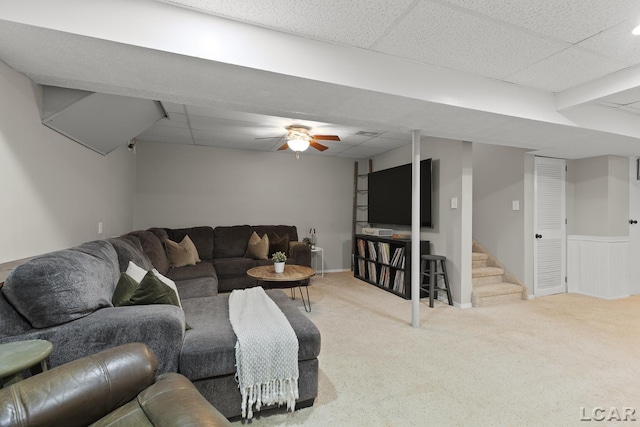 carpeted living area with a drop ceiling, stairs, and a ceiling fan