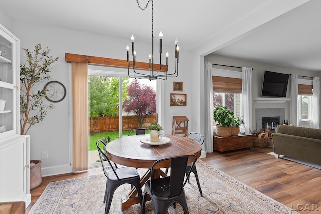 dining area featuring a chandelier, wood finished floors, a glass covered fireplace, and baseboards