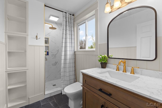 full bathroom with toilet, tiled shower, vanity, wainscoting, and marble finish flooring