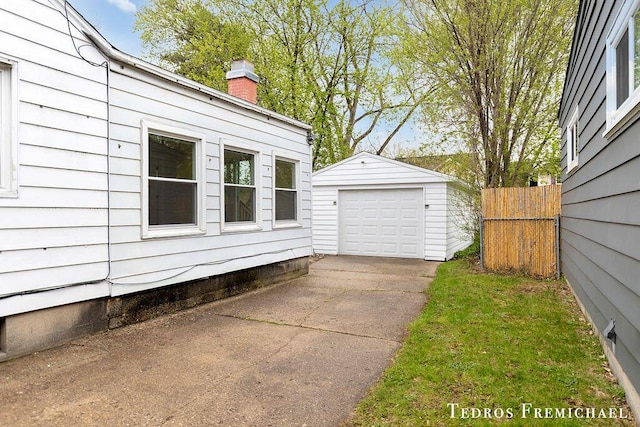 view of side of property with an outbuilding, a chimney, fence, concrete driveway, and a detached garage