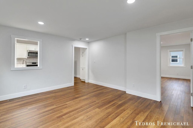 spare room featuring wood finished floors, baseboards, recessed lighting, and a sink