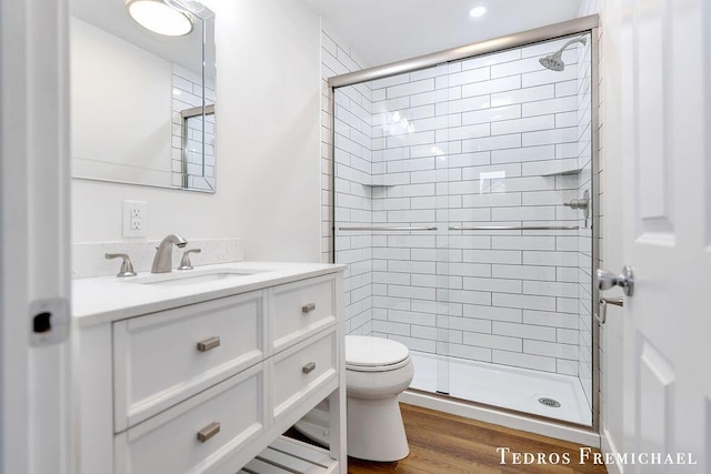 bathroom with a stall shower, toilet, vanity, and wood finished floors
