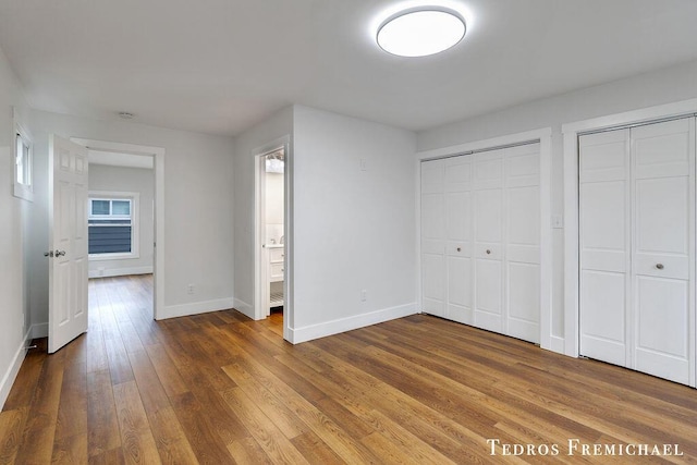 unfurnished bedroom featuring baseboards, hardwood / wood-style flooring, and multiple closets