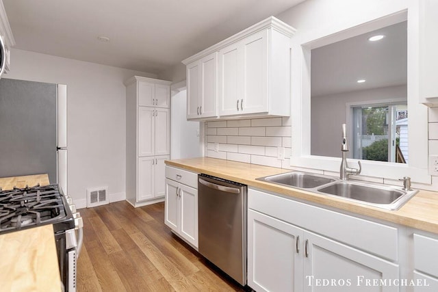 kitchen with appliances with stainless steel finishes, a sink, wooden counters, white cabinets, and tasteful backsplash