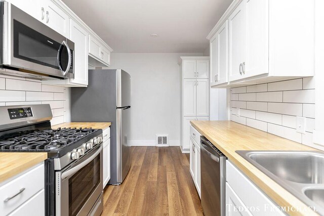 kitchen featuring appliances with stainless steel finishes, wood counters, white cabinetry, a sink, and wood finished floors