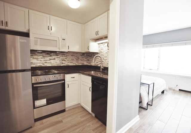kitchen with appliances with stainless steel finishes, a sink, dark countertops, decorative backsplash, and light wood-style floors