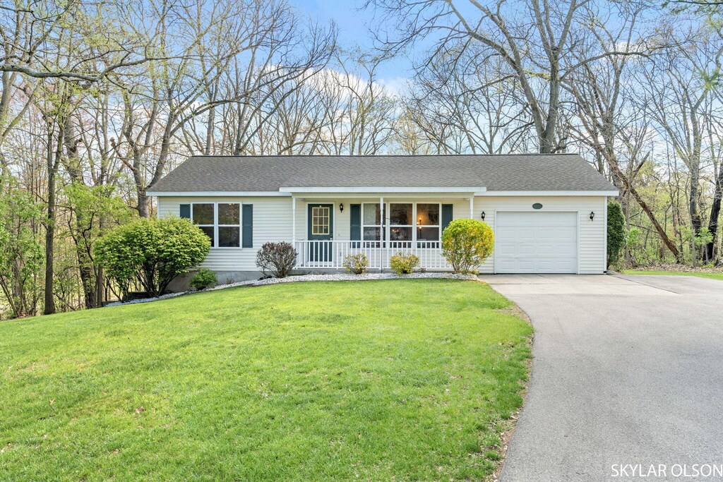 ranch-style house featuring covered porch, asphalt driveway, a garage, and a front yard