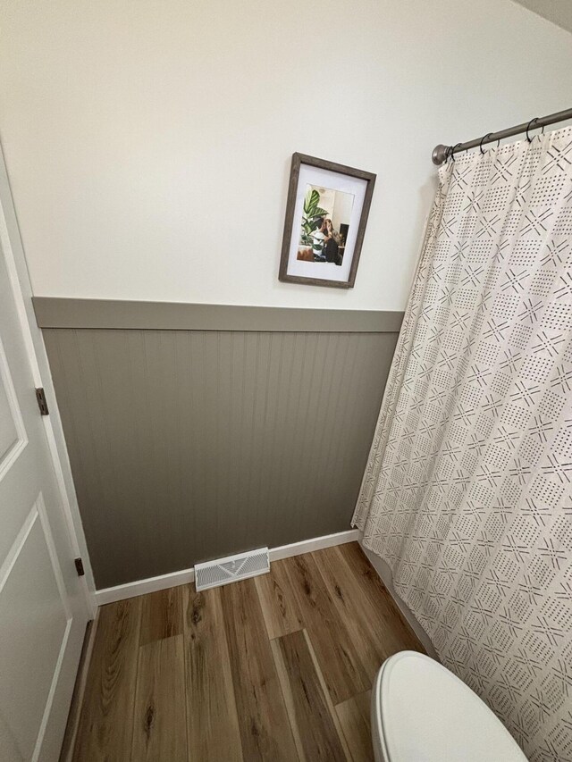 1335 N Sherman Rd, Ludington, MI 49431 - bathroom featuring wood finished floors, wainscoting, toilet, and a shower with shower curtain