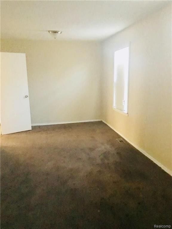 unfurnished room featuring dark colored carpet and baseboards