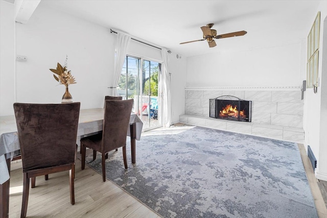 dining space with wood finished floors, a ceiling fan, and a fireplace