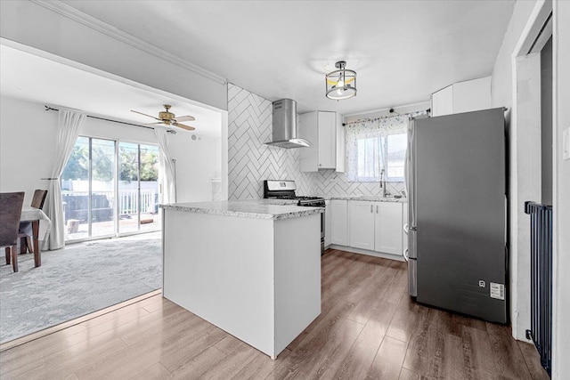 kitchen featuring stainless steel appliances, wall chimney range hood, white cabinetry, a sink, and ornamental molding