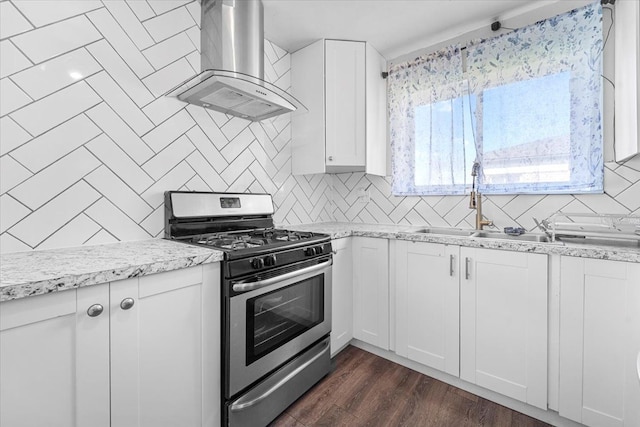 kitchen featuring stainless steel gas stove, wall chimney exhaust hood, decorative backsplash, and white cabinetry