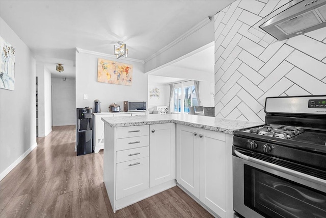 kitchen featuring stainless steel appliances, wall chimney range hood, light stone counters, decorative backsplash, and ornamental molding