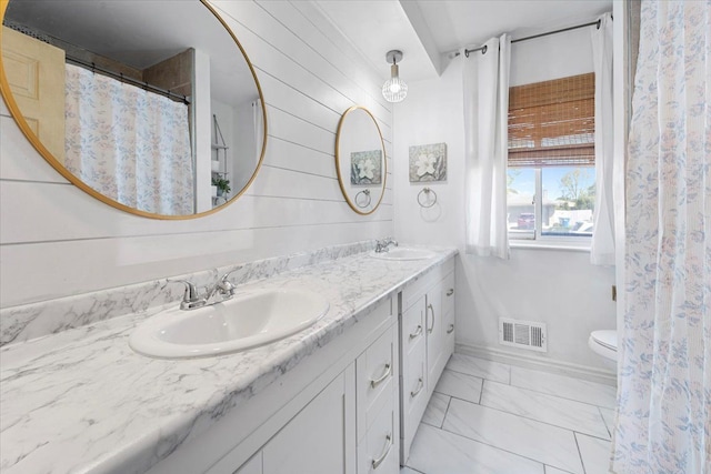 bathroom featuring marble finish flooring, double vanity, toilet, baseboards, and wood walls