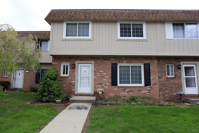 townhome / multi-family property with a front yard, brick siding, and a shingled roof