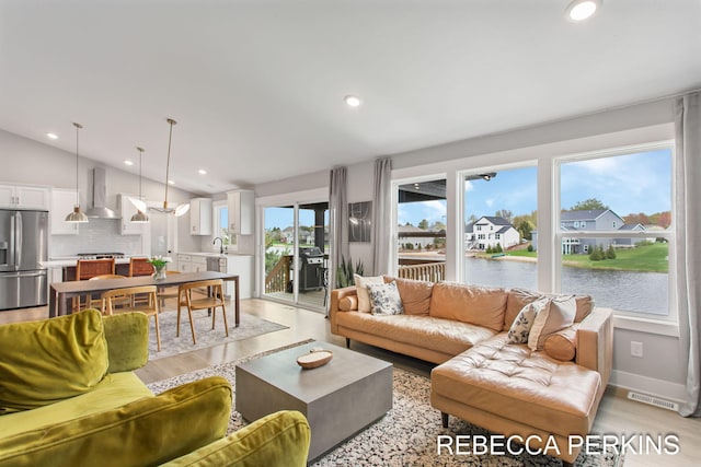living room with lofted ceiling, light wood-style flooring, a water view, and recessed lighting