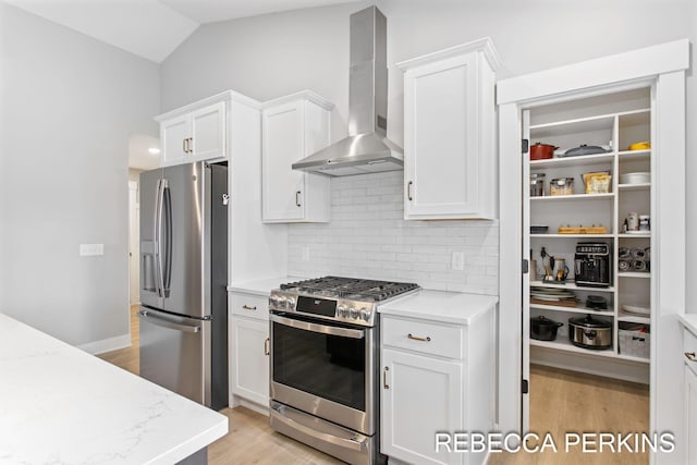 kitchen with appliances with stainless steel finishes, wall chimney exhaust hood, backsplash, light wood-style floors, and white cabinetry