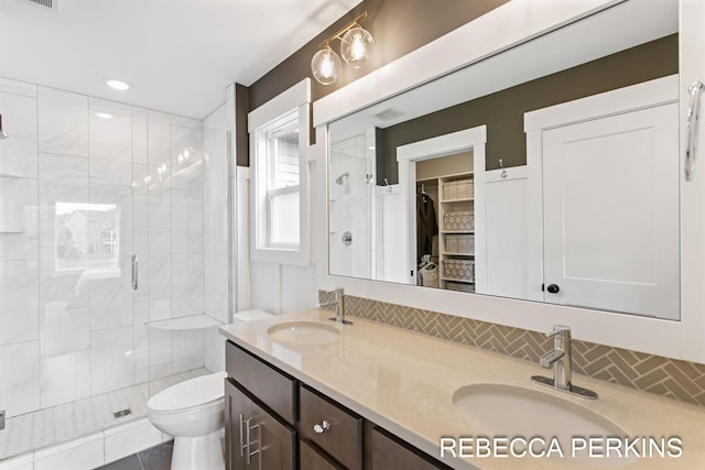 bathroom with a shower stall, toilet, double vanity, and a walk in closet