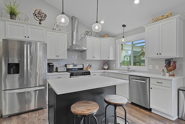 kitchen with appliances with stainless steel finishes, a sink, wall chimney exhaust hood, vaulted ceiling, and white cabinets