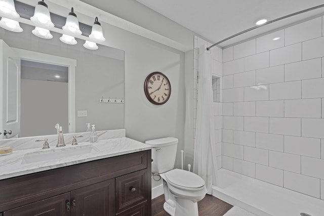 bathroom with toilet, wood finished floors, a tile shower, and vanity