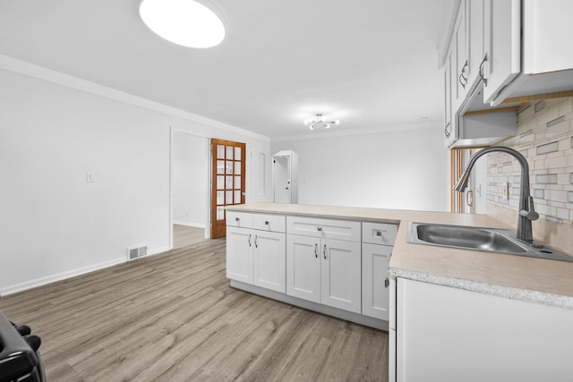 839 E Hayes Ave, Hazel Park, MI 48030 - kitchen featuring a sink, a peninsula, light countertops, tasteful backsplash, and light wood-style flooring