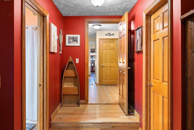 corridor with a textured ceiling, baseboards, and light wood finished floors