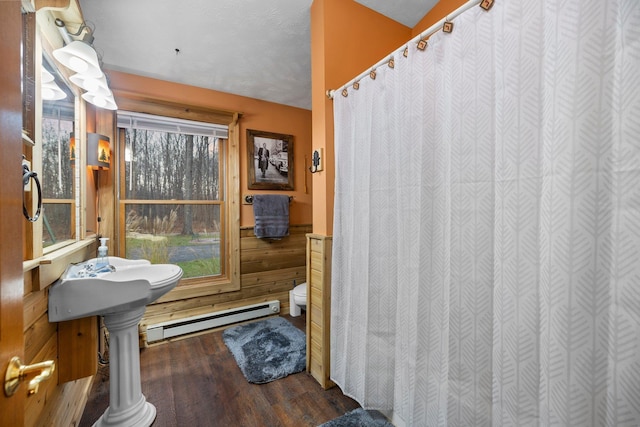 bathroom featuring a baseboard heating unit, wood finished floors, toilet, a wainscoted wall, and curtained shower
