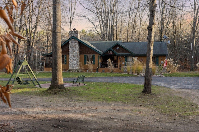 view of front of home featuring a chimney, a lawn, and asphalt driveway